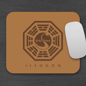 May include: A brown mouse mat with the Dharma Initiative logo and the numbers 4, 8, 15, 16, 23, and 42. A white computer mouse is to the right. The mouse mat is rectangular with rounded corners. Ideal for a computer setup.