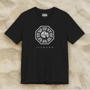 Black short-sleeve t-shirt featuring the Dharma Initiative swan logo graphic from the TV show LOST in a vintage distressed style.