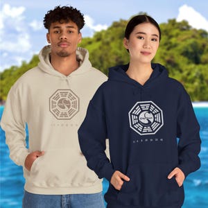 May include: Two hooded sweatshirts with a white Dharma Initiative logo and numbers on the front. The sweatshirt on the left is beige and the sweatshirt on the right is navy blue.