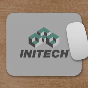 May include: A gray rectangular mousepad with rounded corners. The mousepad features the word "INITECH" in dark gray, below a teal and gray geometric design. A white computer mouse is positioned on the right side of the mousepad.
