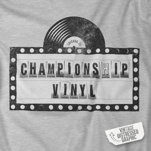 Op de afbeelding: Een grijze t-shirt met een distressed graphic. Het ontwerp bevat de woorden "CHAMPIONSHIP VINYL" in een marquee-stijl, met een vinylplaat erboven. De tekst "Chicago, IL" staat op de plaat. Een vintage distressed graphic staat in de hoek.