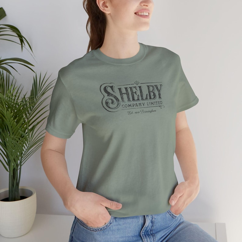 Woman wearing sage green Bella+Canvas 3001 t-shirt featuring a vintage Shelby Company Limited logo from Peaky Blinders.