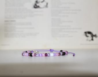 May include: A purple and pink beaded bracelet with a white bead in the centre.