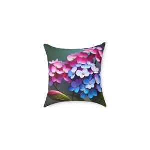 Puede incluir: Cojín cuadrado con diseño floral. El cojín muestra un grupo de flores de hortensia rosas, azules y blancas sobre un fondo verde oscuro. Las flores están detalladas con un efecto pictórico, agregando profundidad y textura al diseño.