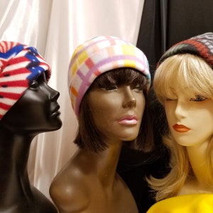 May include: Three mannequins wearing different patterned fleece hats. The hats are red and white, pink and yellow, and black, red, and green.
