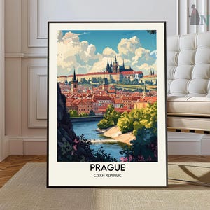 Pode incluir: Uma impressão artística emoldurada de Praga, República Tcheca. A imagem retrata uma paisagem urbana colorida com telhados vermelhos, um rio e um castelo sob um céu azul com nuvens fofas. A palavra "PRAGUE" é impressa em negrito na parte inferior.