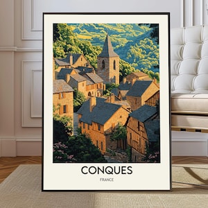 May include: A framed art print featuring a picturesque village scene. The image showcases stone buildings with dark rooftops, a tall church steeple, and lush green hills. The word "CONQUES" and "FRANCE" are printed at the bottom.