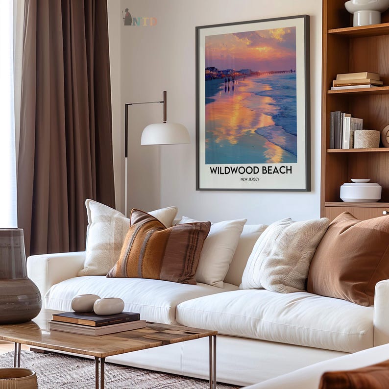 K&ouml;nnte beinhalten: Ein gerahmter Kunstdruck von Wildwood Beach, New Jersey, mit einem Sonnenuntergang &uuml;ber dem Meer. Der Druck wird &uuml;ber einem wei&szlig;en Sofa mit dekorativen Kissen in einem Wohnzimmer gezeigt. Der Raum umfasst auch einen Holztisch und eine Stehlampe.