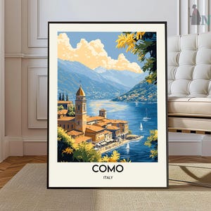Peut inclure: Une affiche encadrée représentant une vue panoramique de Côme, en Italie. L'œuvre d'art dépeint un lac avec des voiliers, des bâtiments et des montagnes sous un ciel bleu avec des nuages jaunes. Les mots "COMO" et "ITALY" sont imprimés en bas.