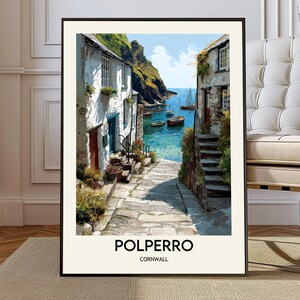 Pode incluir: Uma impressão artística emoldurada de Polperro, Cornualha. A imagem retrata uma cena costeira com edifícios brancos, um caminho de pedra e barcos na água turquesa. O céu é azul e a impressão está numa moldura preta.