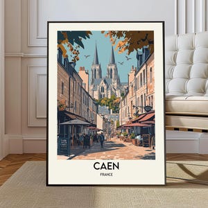 Può includere: Una stampa artistica incorniciata con una scena di strada a Caen, in Francia. L'opera raffigura una via di una città europea con edifici, negozi e una cattedrale sullo sfondo. La stampa ha una cornice nera e il testo "CAEN FRANCE" in basso.