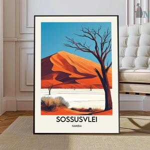 May include: A framed art print depicting a desert scene with an orange sand dune under a blue sky. A bare tree is in the foreground. The print has the text "Sossusvlei Namibia" at the bottom.