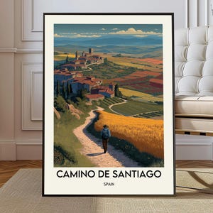 May include: A framed art print of the Camino de Santiago in Spain. The artwork depicts a person walking on a path towards a village, with fields and mountains in the background. The text "CAMINO DE SANTIAGO" and "SPAIN" are at the bottom.