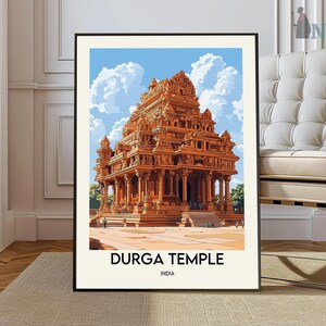 May include: A framed print featuring the Durga Temple in India. The artwork depicts the temple in shades of orange and brown, set against a blue sky with fluffy white clouds. The text "DURGA TEMPLE INDIA" is displayed at the bottom.