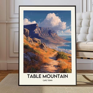 May include: A framed print of Table Mountain in Cape Town. The artwork depicts a scenic landscape with a mountain, ocean, and a path. The sky is blue with fluffy white clouds. The text "TABLE MOUNTAIN CAPE TOWN" is at the bottom.