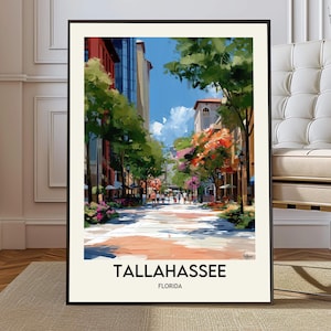 May include: A framed art print of Tallahassee, Florida. The artwork depicts a colorful street scene with buildings, trees, and pedestrians. The word "TALLAHASSEE" is printed in bold black letters at the bottom, with "FLORIDA" below it.