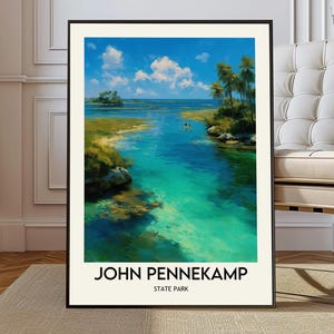 Op de afbeelding: Een ingelijste kunstdruk van John Pennekamp State Park. Het kunstwerk toont een levendige kustscène met turquoise water, weelderige groene vegetatie en een helderblauwe lucht bezaaid met pluizige witte wolken. De tekst "JOHN PENNEKAMP STATE PARK" staat onderaan afgedrukt.