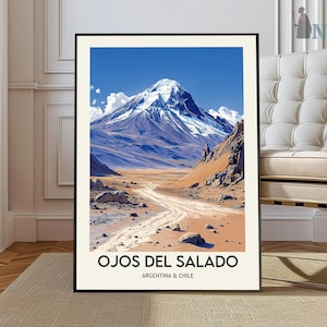 May include: A framed art print featuring a mountain landscape under a bright blue sky with white clouds. The artwork depicts a dirt road leading towards the mountain. The text "OJOS DEL SALADO ARGENTINA & CHILE" is printed at the bottom.