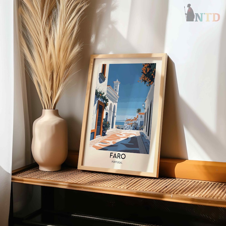 May include: A framed print of a colorful illustration of a street scene in Faro, Portugal. The illustration features white buildings with blue accents, a blue sky, and a cobblestone street.