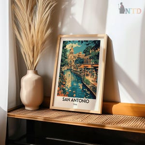 May include: A framed print of a colorful painting depicting a canal in San Antonio, Texas. The painting features a blue canal with buildings and trees on either side. The canal is filled with water and there are people walking along the banks. The print is framed in a wooden frame.