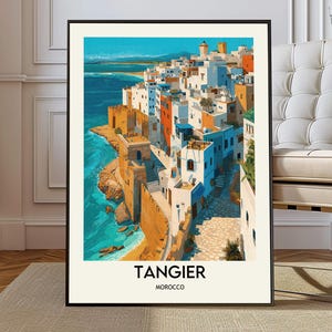 Può includere: Una stampa artistica incorniciata raffigurante una scena di città costiera. L'opera d'arte mostra edifici bianchi con dettagli arancioni e blu lungo un mare turchese. Il testo "TANGERI MAROCCO" è stampato in basso.