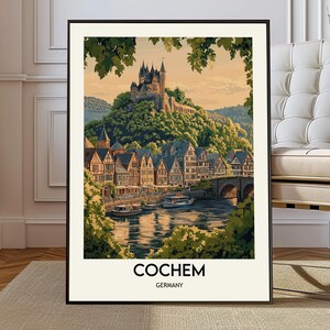 May include: Framed art print of Cochem, Germany. The print depicts a picturesque view of a town with a castle atop a hill, a river, and a bridge. The print has a black frame and the text "Cochem Germany" at the bottom.