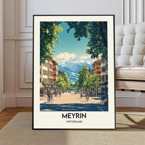 May include: A framed art print depicting a street scene in Meyrin, Switzerland. The artwork features a sunny day with cyclists, buildings, and a mountain range in the background. The print has a black frame and the text "MEYRIN SWITZERLAND" at the bottom.