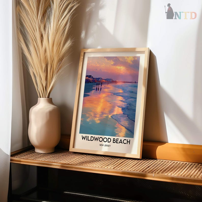 K&ouml;nnte beinhalten: Ein gerahmter Druck von Wildwood Beach, New Jersey, mit einem lebendigen Sonnenuntergang &uuml;ber dem Meer. Das Kunstwerk befindet sich in einem hellen Holzrahmen und steht auf einem gewebten Regal. Links befindet sich eine beige Vase mit hohem, getrocknetem Gras.