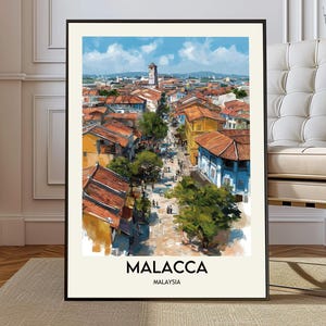 Può includere: Una stampa incorniciata di Malacca, Malesia, con una rappresentazione in stile acquerello di una scena di strada cittadina. L'opera presenta edifici con tetti arancioni, un cielo blu e il testo "MALACCA MALAYSIA" in basso.