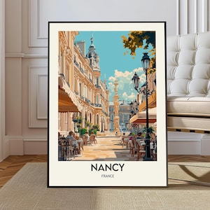 May include: A framed art print of a street scene in Nancy, France. The artwork depicts a sunny day with people seated at outdoor cafes. Buildings with awnings line the street, and the sky is a bright blue with fluffy white clouds.