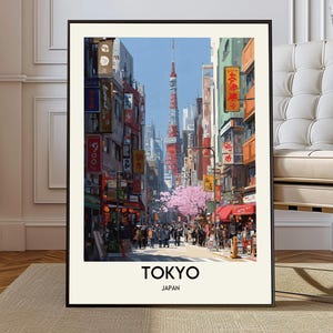 Op de afbeelding: Een ingelijste kunstdruk van een straatbeeld in Tokio, met de Tokyo Tower op de achtergrond. Het kunstwerk toont een drukke straat met winkels, voetgangers en kersenbloesems. De woorden "TOKYO" en "JAPAN" staan onderaan afgedrukt.