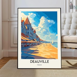 May include: A framed art print of Deauville, France, featuring a colorful illustration of a beach scene. The artwork depicts buildings with orange roofs, blue awnings, a sandy beach, and a bright blue sky with fluffy white clouds. The word "DEAUVILLE" is printed at the bottom.