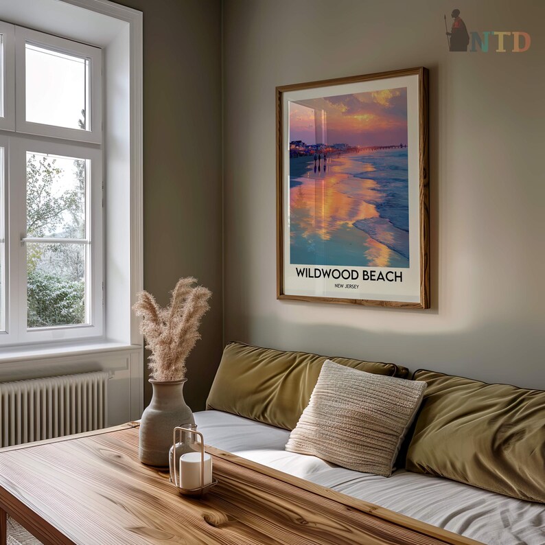K&ouml;nnte beinhalten: Ein gerahmter Druck von Wildwood Beach, New Jersey, mit einem Sonnenuntergang &uuml;ber dem Meer. Das Kunstwerk befindet sich in einem Holzrahmen und h&auml;ngt &uuml;ber einem Sofa mit olivgr&uuml;nen Kissen und einem dekorativen Kissen. Eine Vase mit getrockneten Pflanzen und ein Kerzenhalter stehen auf einem Holztisch.