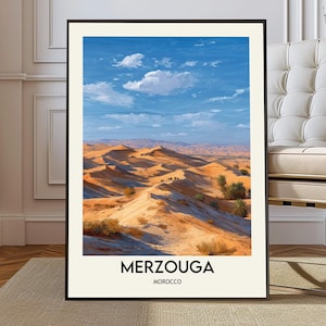 May include: Framed art print featuring a desert landscape under a blue sky with fluffy white clouds. The artwork depicts sand dunes in shades of tan and brown, with the word "MERZOUGA" and "MOROCCO" printed at the bottom.