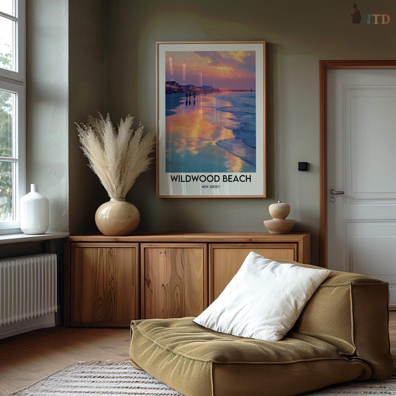 K&ouml;nnte beinhalten: Ein gerahmtes Poster mit den Worten "Wildwood Beach, New Jersey" zeigt eine Strandszene mit einem farbenfrohen Sonnenuntergang. Das Poster h&auml;ngt &uuml;ber einem Holzschrank, neben einer Vase mit hohen, getrockneten Pflanzen. Ein gr&uuml;nes Bodenkissen mit einem wei&szlig;en Kissen befindet sich im Vordergrund.