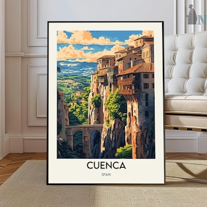 May include: Framed art print of Cuenca, Spain, featuring a vibrant illustration of cliffside buildings, a stone bridge, and lush greenery. The artwork showcases a picturesque landscape under a blue sky with fluffy clouds. The text "CUENCA SPAIN" is at the bottom.