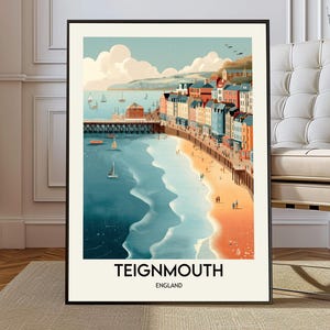 May include: A framed art print of Teignmouth, England, featuring a coastal scene. The artwork depicts a beach with colorful buildings, a pier, and sailboats on the water. The sky is a light blue with fluffy clouds. The print has a black frame.