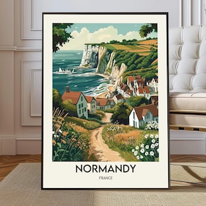 May include: A framed art print of a coastal scene in Normandy, France. The artwork depicts a village nestled along a shoreline with white cliffs, green hills, and a blue ocean. The print has a black frame and the text "NORMANDY FRANCE" at the bottom.