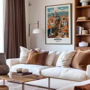 K&ouml;nnte beinhalten: Ein gerahmter Kunstdruck von M&eacute;rida, Venezuela, h&auml;ngt &uuml;ber einem wei&szlig;en Sofa mit dekorativen Kissen. Der Druck zeigt eine farbenfrohe Stadtlandschaft mit Bergkulisse. Ein Holztisch und eine Stehlampe vervollst&auml;ndigen das Wohnzimmer.