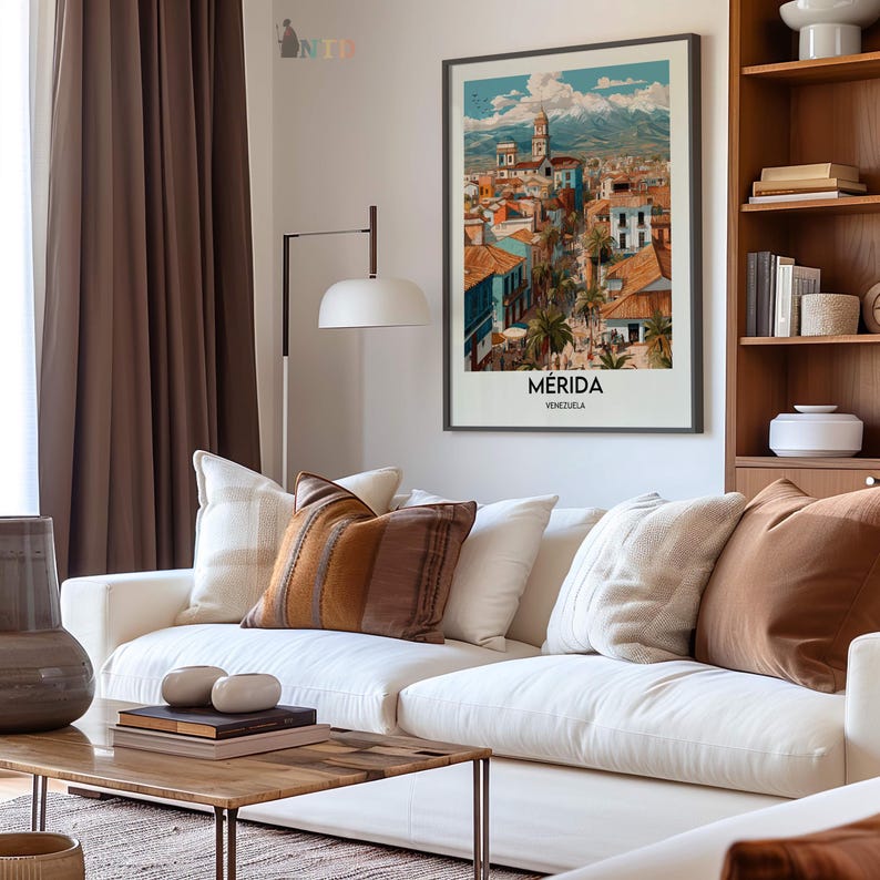 K&ouml;nnte beinhalten: Ein gerahmter Kunstdruck von M&eacute;rida, Venezuela, h&auml;ngt &uuml;ber einem wei&szlig;en Sofa mit dekorativen Kissen. Der Druck zeigt eine farbenfrohe Stadtlandschaft mit Bergkulisse. Ein Holztisch und eine Stehlampe vervollst&auml;ndigen das Wohnzimmer.