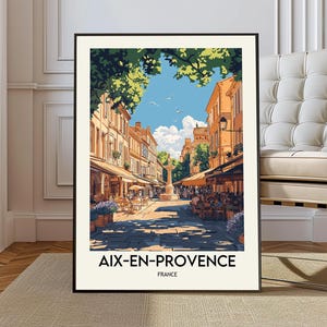 以下が含まれることがあります： フランス、エクス＝アン＝プロヴァンスの街並みが描かれた額入りのアートプリント。 晴れた日に建物、カフェ、噴水が描かれています。 プリントの下部には「AIX-EN-PROVENCE FRANCE」の文字があります。