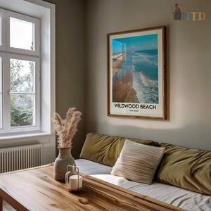 May include: A framed print of Wildwood Beach, New Jersey, hangs on a wall. The print shows a beach scene with blue water, a sandy shore, and the text "Wildwood Beach". The frame is made of wood.