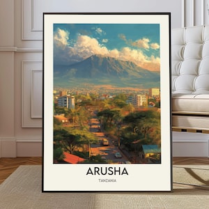 May include: Framed art print featuring a scenic view of Arusha, Tanzania. The artwork depicts a city nestled at the base of a mountain, under a blue sky with fluffy clouds. The word "ARUSHA" is printed in bold white letters at the bottom.