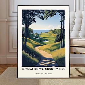 May include: Framed art print of Crystal Downs Country Club in Frankfort, Michigan. The artwork depicts a golf course with a winding path, lush green fairways, and a view of the blue ocean. The print is in a black frame.