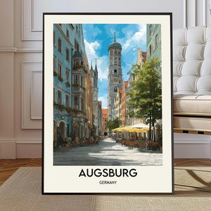 May include: A framed art print showcasing a street scene in Augsburg, Germany. The image displays colourful buildings, a clock tower, and a bright sky. The words "Augsburg" and "Germany" are printed at the bottom of the print.