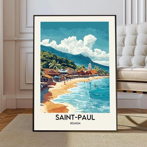 May include: A framed art print featuring a coastal scene with a beach, ocean, and buildings. The artwork depicts a sunny day with blue skies, white clouds, and lush green mountains. The text "SAINT-PAUL RÉUNION" is at the bottom.