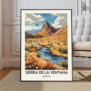 May include: A framed art print featuring a landscape scene of the Sierra de la Ventana in Argentina. The artwork depicts a river flowing through a valley with mountains, wildlife, and a blue sky with clouds. The print is in a black frame.