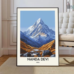 May include: A framed art print featuring a mountain landscape. The artwork depicts a snow-capped peak under a clear blue sky, with valleys in shades of blue and orange. The text "NANDA DEVI INDIA" is printed at the bottom.