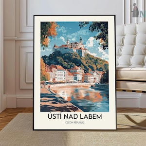 Puede incluir: Una impresión artística enmarcada que presenta una vista panorámica de Ústí nad Labem, República Checa. La obra de arte representa un río, edificios y un castillo en la cima de una colina bajo un cielo azul. La impresión está en un marco negro.