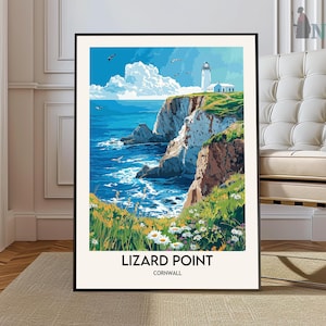May include: A framed print of Lizard Point, Cornwall, featuring a white lighthouse on a cliff overlooking a blue sea. The artwork includes green grass, white cliffs, and a bright blue sky with clouds. The text "LIZARD POINT CORNWALL" is at the bottom.